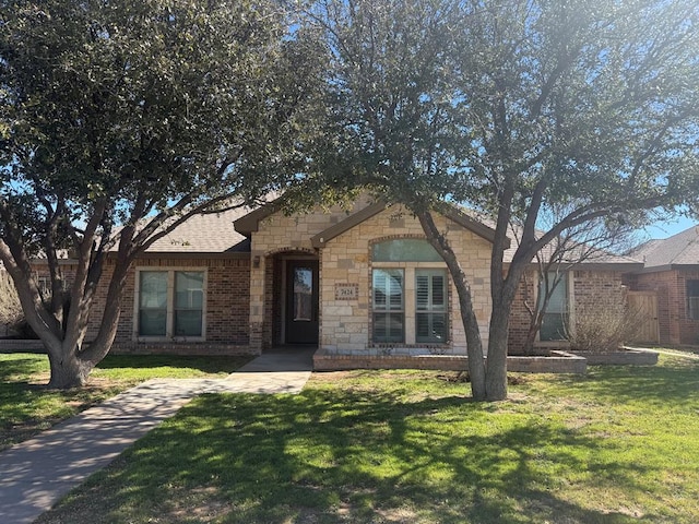 ranch-style home featuring stone siding, brick siding, roof with shingles, and a front yard