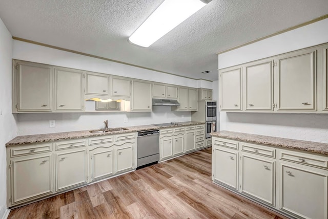 kitchen with appliances with stainless steel finishes, sink, light stone counters, a textured ceiling, and light hardwood / wood-style flooring