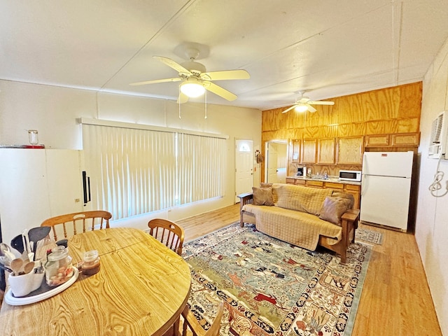 living room featuring ceiling fan, light wood-type flooring, and wooden walls