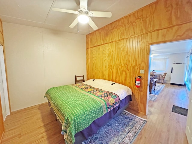 bedroom with hardwood / wood-style flooring, ceiling fan, wood walls, and white refrigerator