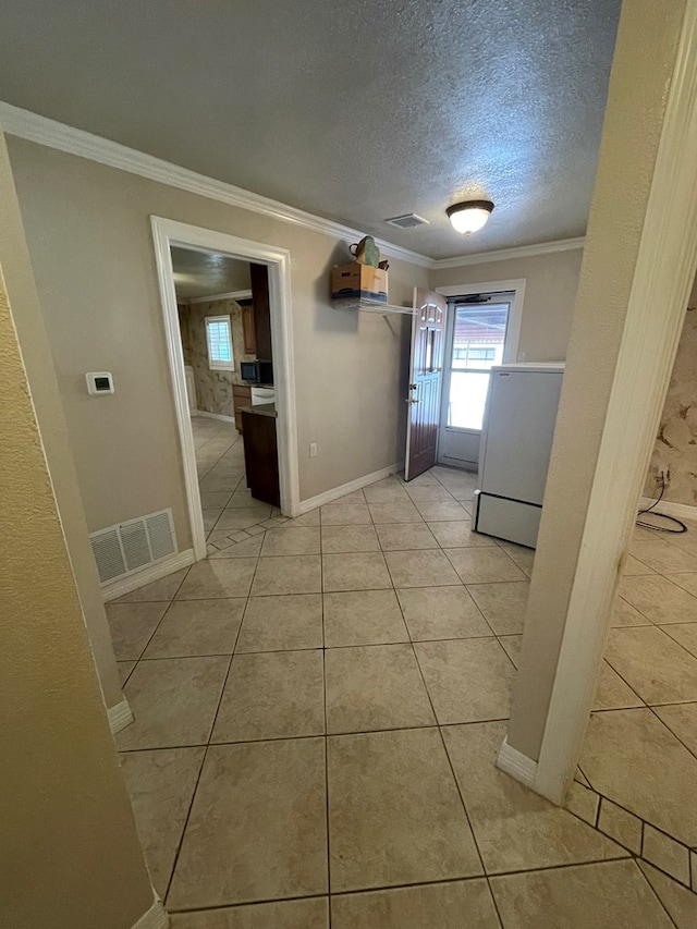 hallway with a textured ceiling, light tile patterned floors, and crown molding