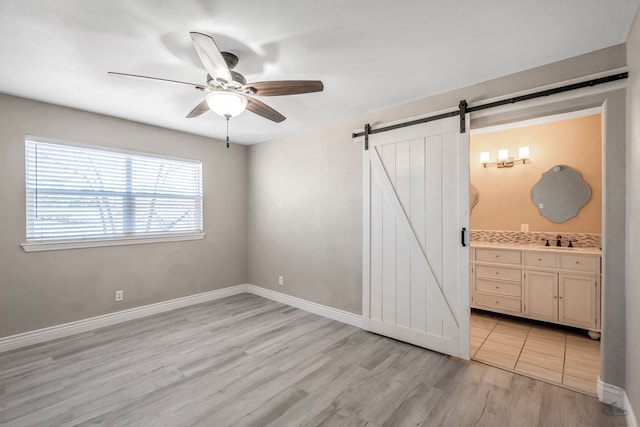 unfurnished bedroom featuring light wood-style flooring, ensuite bathroom, a barn door, a sink, and baseboards