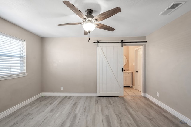 unfurnished bedroom with a barn door, visible vents, baseboards, a ceiling fan, and light wood-style flooring