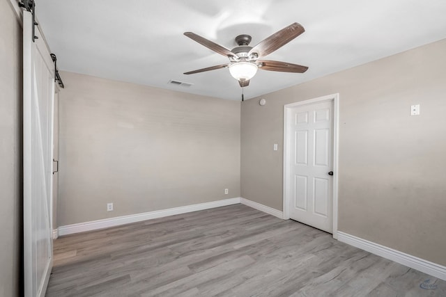 empty room with a barn door, visible vents, baseboards, a ceiling fan, and wood finished floors