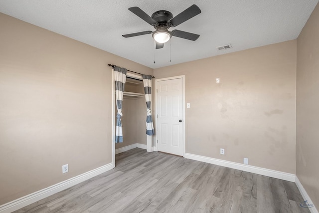 empty room with light wood-style floors, baseboards, visible vents, and a textured ceiling