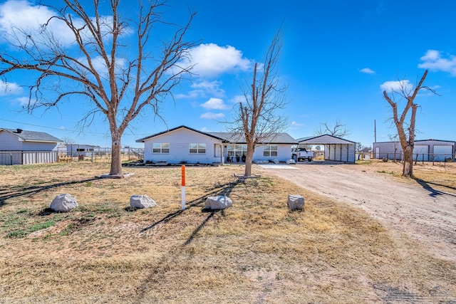 ranch-style house with dirt driveway, fence, and a detached carport