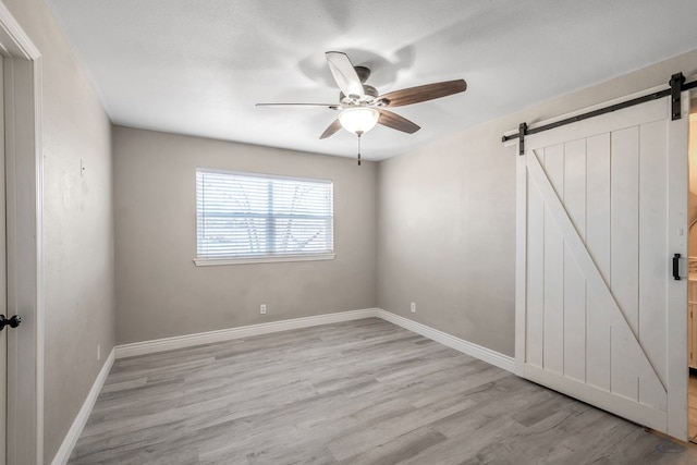 empty room with a barn door, baseboards, a ceiling fan, light wood-style flooring, and a textured ceiling