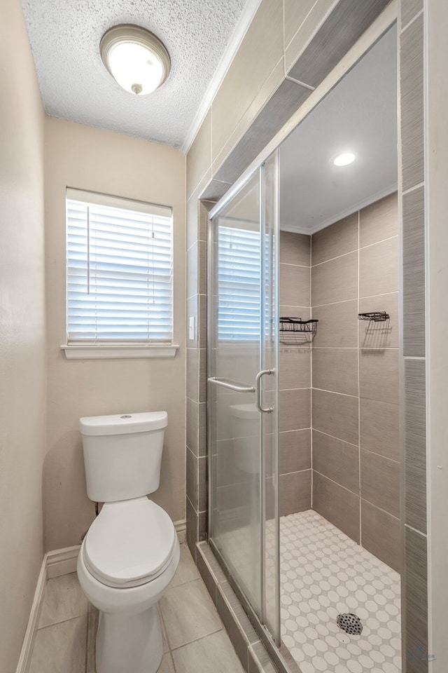 bathroom featuring toilet, a shower stall, a textured ceiling, tile patterned flooring, and baseboards