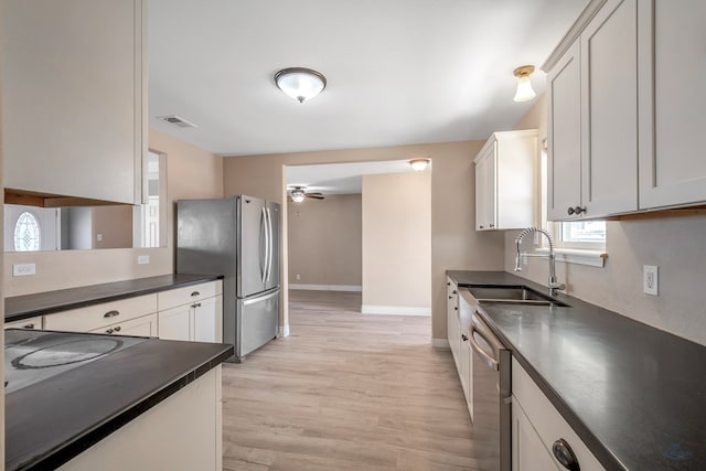 kitchen with light wood finished floors, dark countertops, visible vents, appliances with stainless steel finishes, and a sink