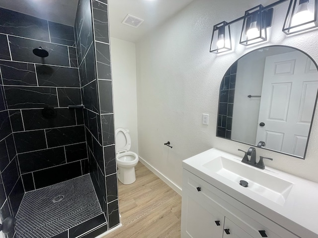 bathroom with tiled shower, wood-type flooring, vanity, and toilet