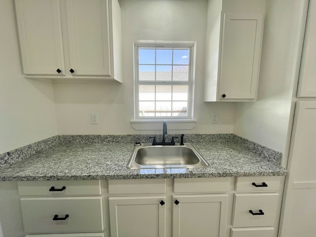 kitchen with white cabinetry, sink, and light stone counters