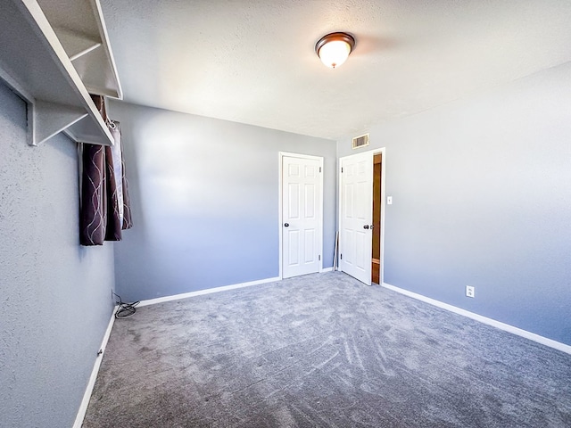 spare room with carpet floors, visible vents, a textured ceiling, and baseboards