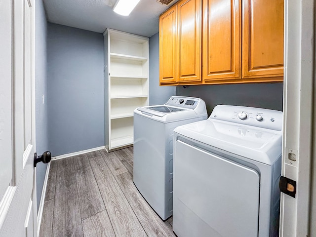 laundry area with cabinet space, light wood-style flooring, baseboards, and separate washer and dryer