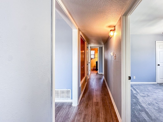 hallway featuring baseboards, visible vents, a textured wall, dark wood-style flooring, and a textured ceiling