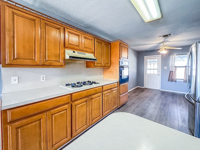 kitchen featuring white gas stovetop, brown cabinetry, freestanding refrigerator, black oven, and under cabinet range hood