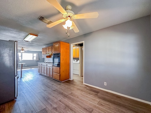 kitchen with washer and clothes dryer, visible vents, dark wood-type flooring, freestanding refrigerator, and black oven