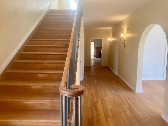 stairs featuring arched walkways, wood finished floors, and baseboards