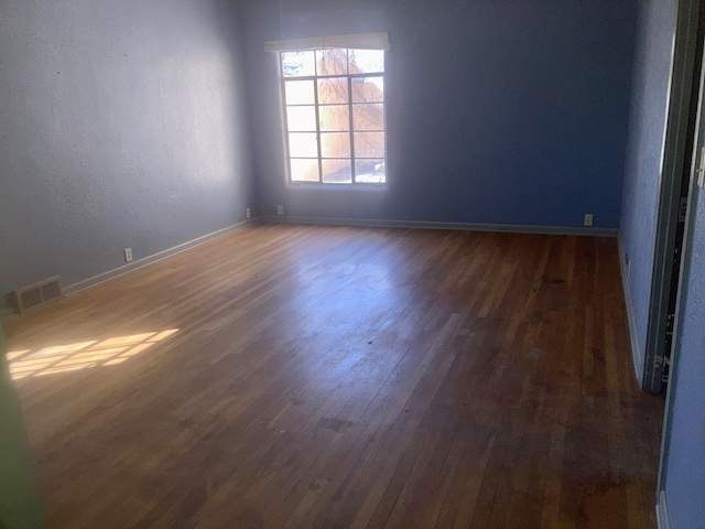 empty room with wood finished floors, visible vents, and baseboards