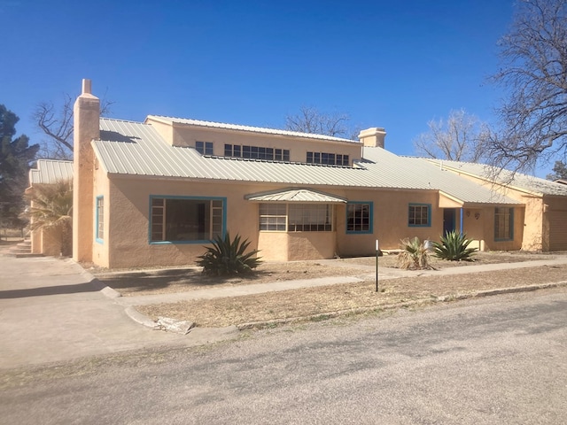 view of front of home with metal roof, a chimney, and stucco siding