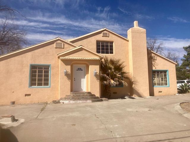 view of front facade featuring crawl space, a chimney, and stucco siding