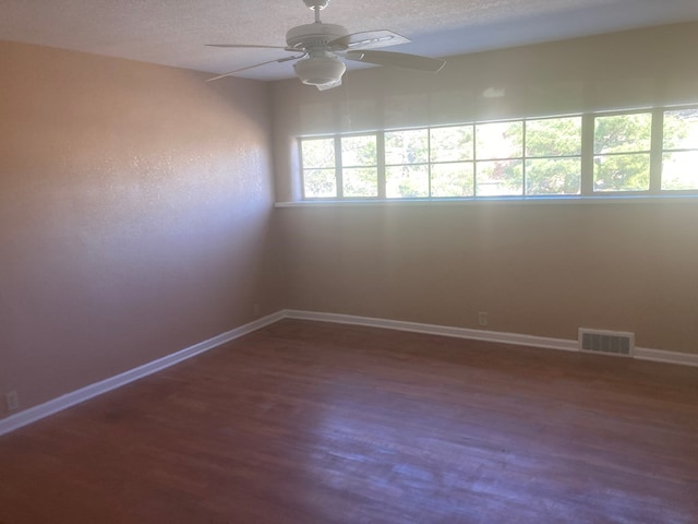 unfurnished room with a textured ceiling, wood finished floors, a ceiling fan, visible vents, and baseboards