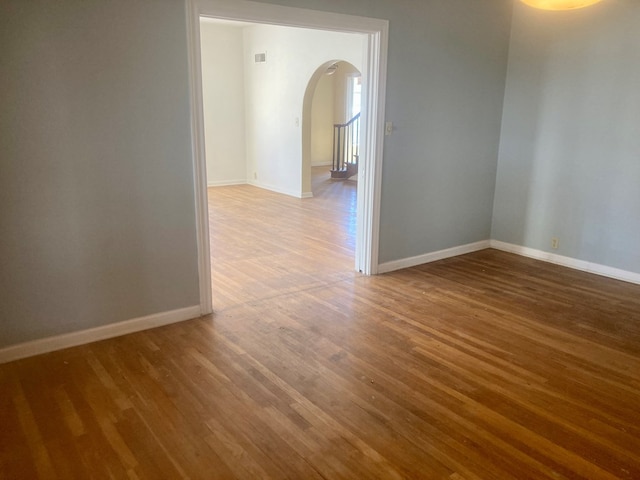 unfurnished room featuring baseboards, visible vents, arched walkways, and wood finished floors