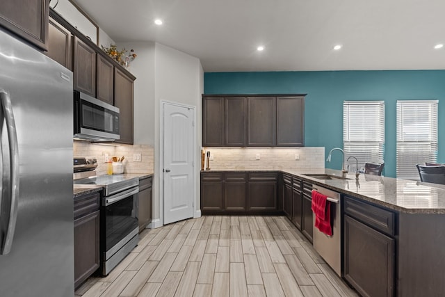 kitchen featuring kitchen peninsula, light stone countertops, stainless steel appliances, decorative backsplash, and sink