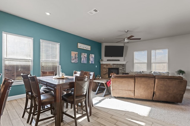 dining room with ceiling fan and a stone fireplace