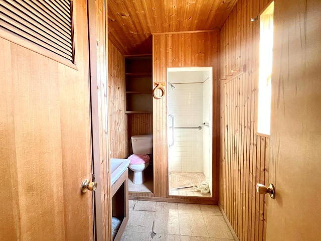 bathroom with tiled shower, wooden walls, toilet, and wooden ceiling