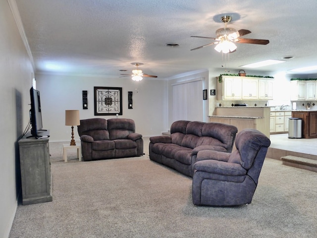 living room featuring a textured ceiling, ornamental molding, ceiling fan, and light colored carpet