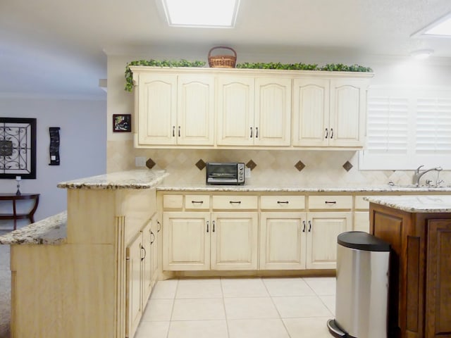 kitchen with light tile patterned floors, a peninsula, ornamental molding, and light stone countertops