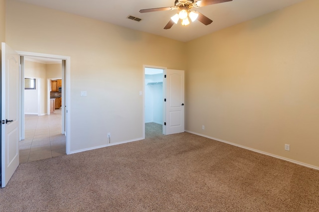 unfurnished bedroom featuring ceiling fan, light colored carpet, and a walk in closet