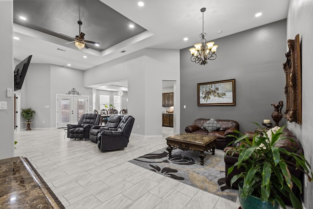 living area with baseboards, a towering ceiling, a tray ceiling, ceiling fan with notable chandelier, and recessed lighting