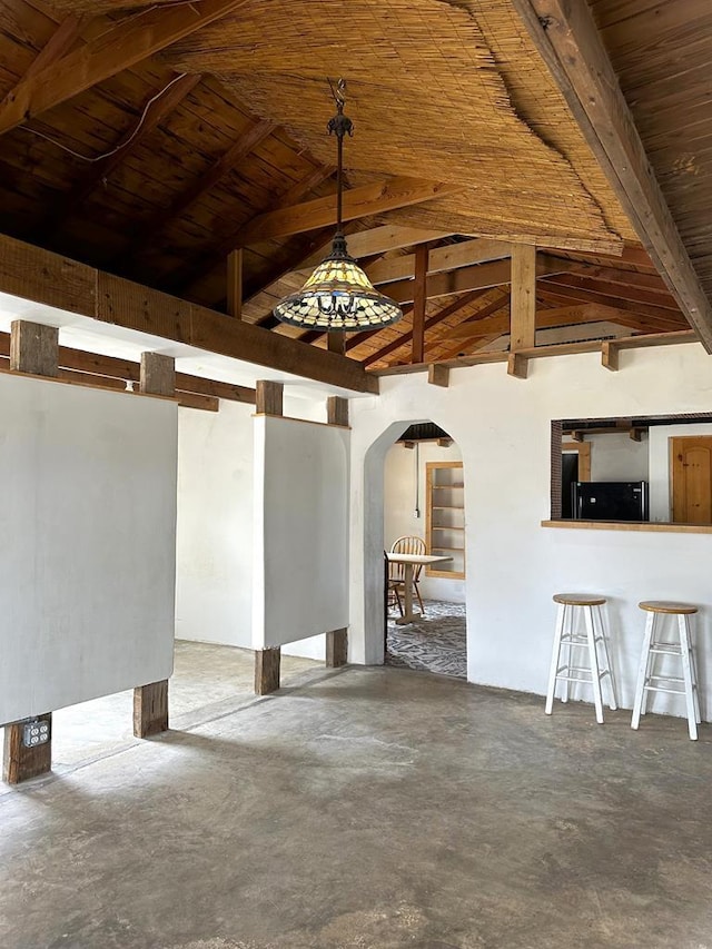 empty room with arched walkways, concrete floors, wooden ceiling, and beam ceiling