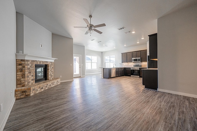 kitchen featuring ceiling fan, stainless steel appliances, dark wood-type flooring, and a fireplace