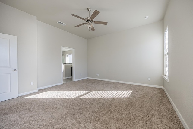 empty room with a wealth of natural light, ceiling fan, vaulted ceiling, and light colored carpet