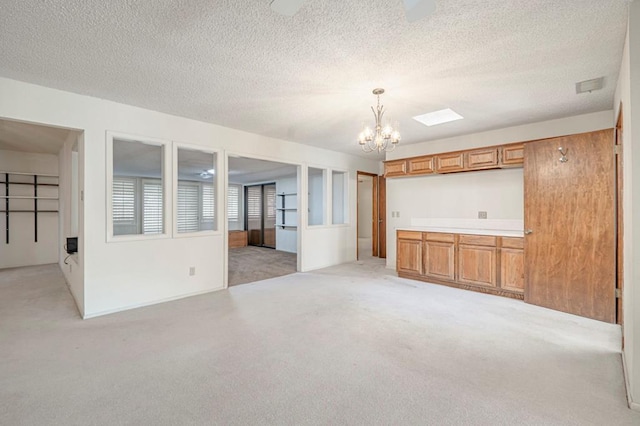 unfurnished living room featuring light colored carpet, a textured ceiling, and a notable chandelier