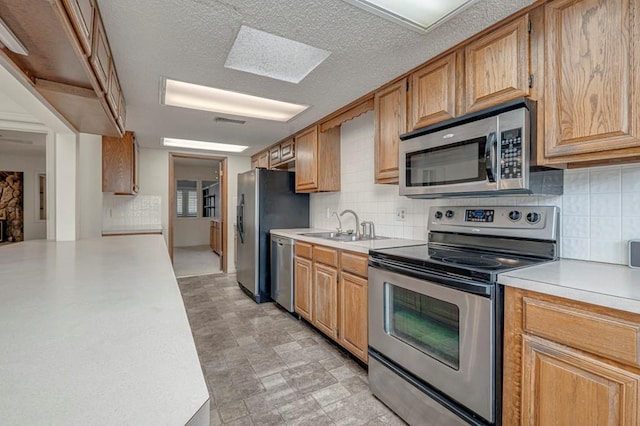 kitchen with appliances with stainless steel finishes, backsplash, a skylight, a textured ceiling, and sink