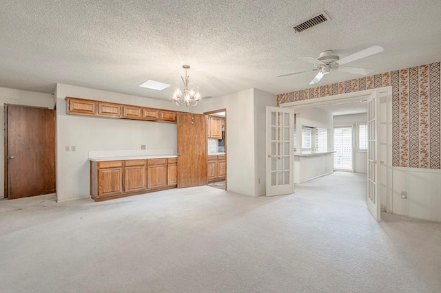 unfurnished living room with a textured ceiling, ceiling fan with notable chandelier, and light colored carpet