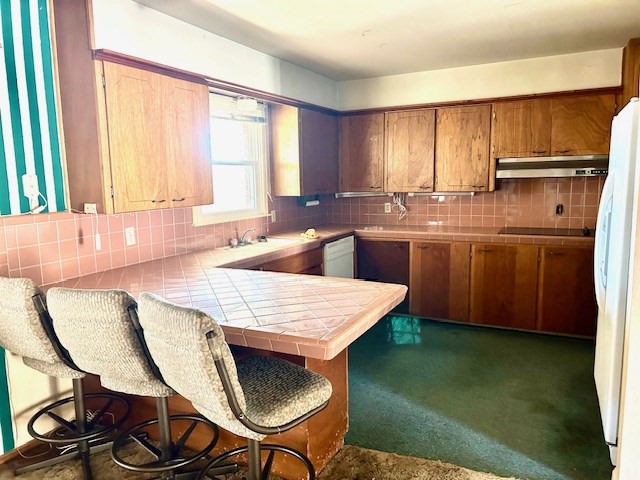 kitchen featuring tile counters, sink, tasteful backsplash, white appliances, and a kitchen bar