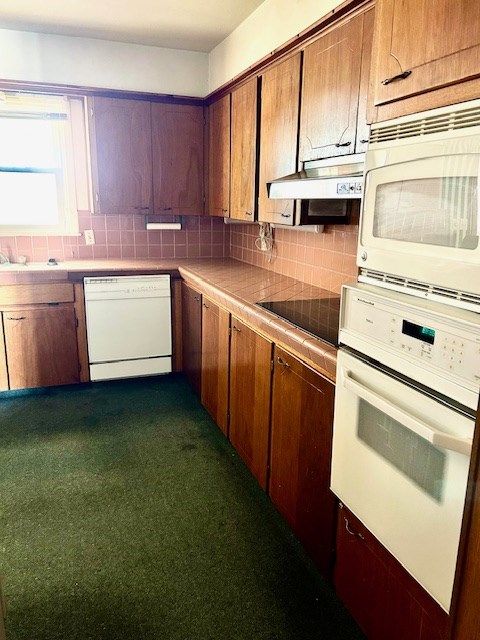 kitchen with tile counters, decorative backsplash, white appliances, and sink