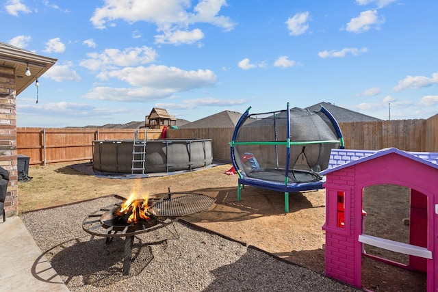 view of yard featuring a fenced in pool, a trampoline, and an outdoor fire pit