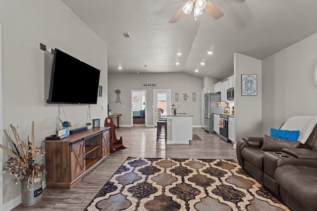 living room with lofted ceiling, sink, ceiling fan, a textured ceiling, and light hardwood / wood-style flooring