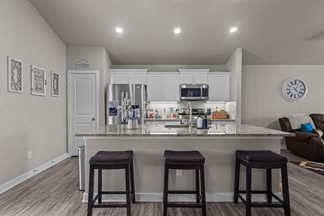 kitchen featuring a kitchen island with sink, stainless steel appliances, white cabinets, and a kitchen bar