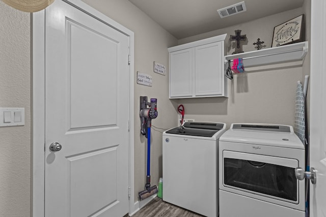 washroom with hardwood / wood-style floors, washing machine and dryer, and cabinets