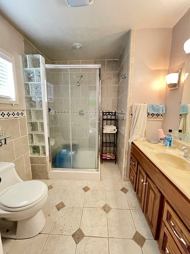 bathroom with vanity, a shower with door, tile patterned floors, toilet, and tile walls