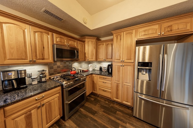 kitchen with dark wood-style flooring, visible vents, backsplash, appliances with stainless steel finishes, and dark stone countertops