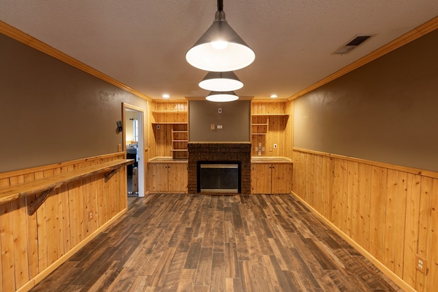 unfurnished living room with a fireplace, visible vents, ornamental molding, wainscoting, and wood finished floors