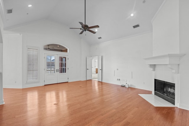 unfurnished living room with light hardwood / wood-style floors, french doors, crown molding, and a tiled fireplace