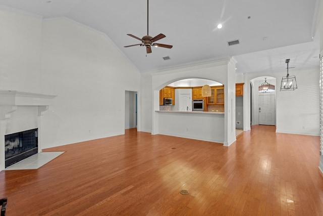 unfurnished living room with ceiling fan, crown molding, a tiled fireplace, and light wood-type flooring